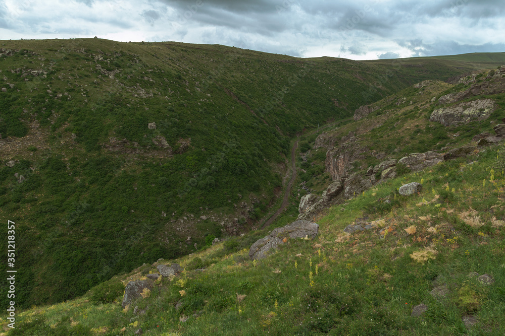 From above of rural winding road in hilly area. Dirt curve road in mountains near green meadows From above of rural winding road in hilly area. Dirt curve road in mountains near green meadows