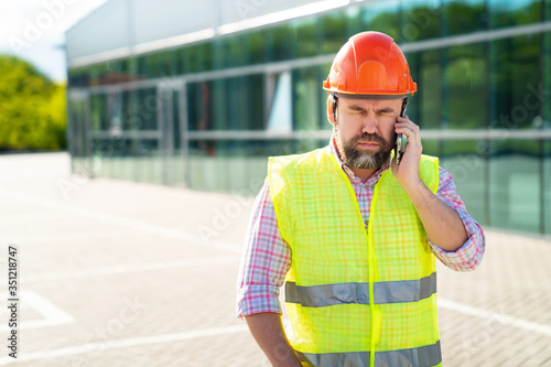 upset man construction superintendent in construction helmet answers phone call