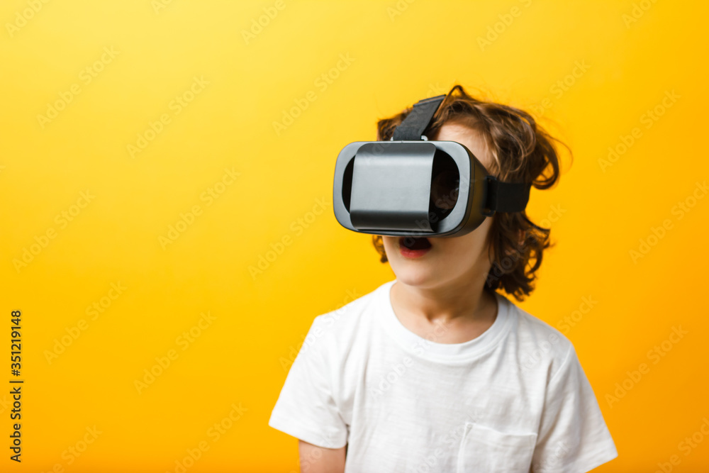 Fototapeta premium Close-up of little boy in virtual reality headset. Boy wearing virtual reality glasses white tshirt at yellow background