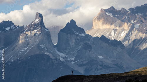 Huge mountains panorama in blue tones and cloudy sky with a silhouette of a man standing in the foreground. 