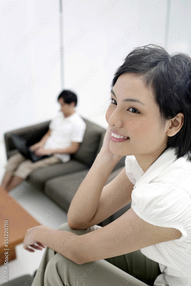 Woman talking on the mobile phone, man using laptop in the background Woman talking on the mobile phone, man using laptop in the background