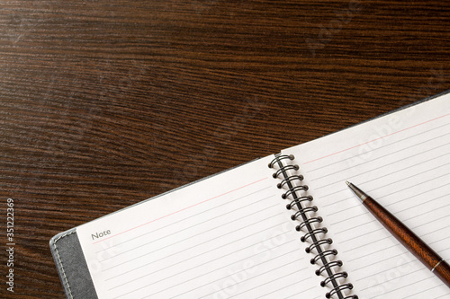 An open notebook with empty pages and a pen for writing on a table of brown wood. photo