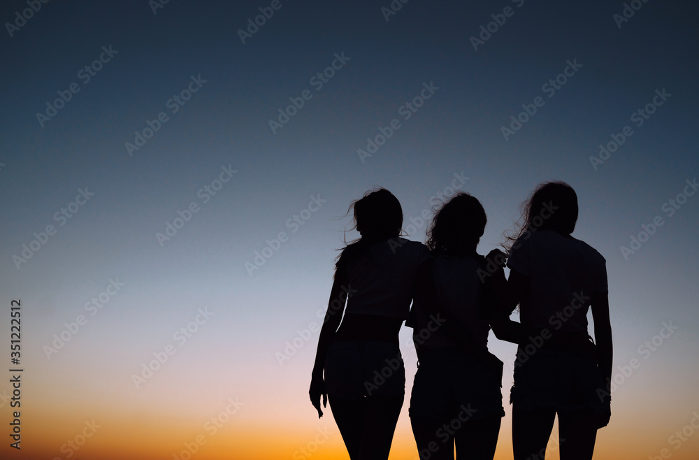Silhouette of three young girls standing  on the beach and looking to a sunset. Summer holidays, vacation, relax and lifestyle concept.