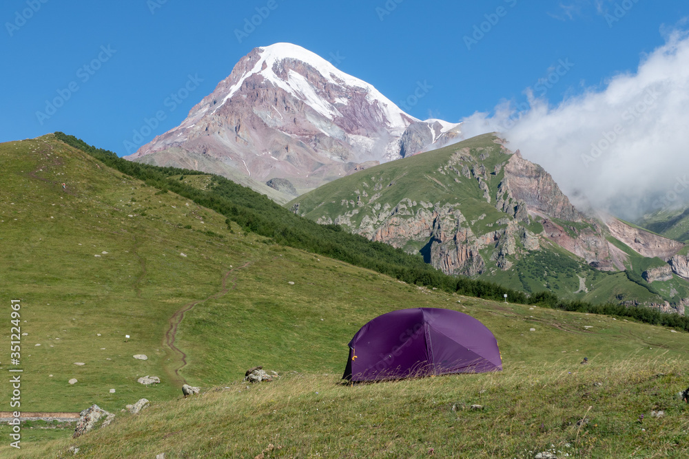 touristic tent in front of spectacular view of magnificent  kazbek mountain with snow peak in caucasus in geogria. breathtaking view, traveling in beautiful places