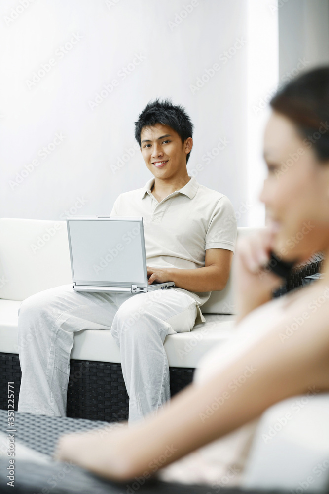 Woman talking on the mobile phone with man using laptop in the background Woman talking on the mobile phone with man using laptop in the background