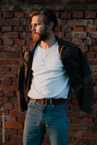 Bearded man posing against a brick wall.