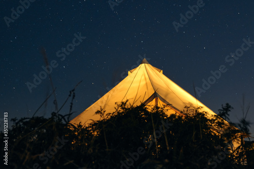 Glamping illuminated from the inside against a starry sky on a summer night. Camping and outdoor concept.