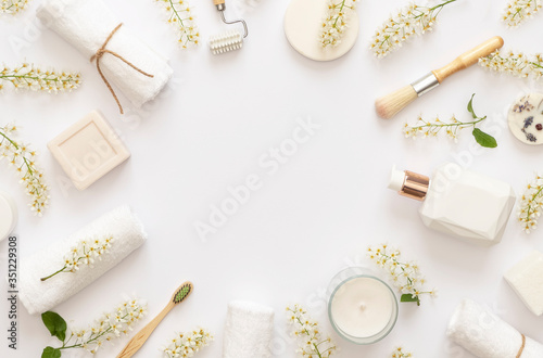 Stylish White Spa concept. Flowering branches of bird cherry on white baground. White candle, soap, cream, towels. Copy space. Flat lay. 