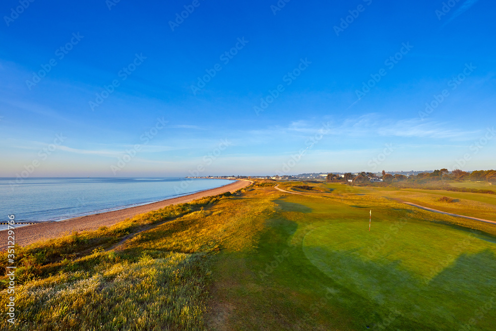 Image of Grouville bay with the common, beach and sea with blue sky at sunrise. Jersey, Channel Islands, UK