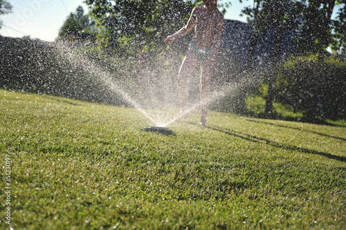 child plays with water sprayer in the garden, summer background