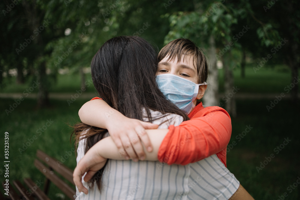 Naklejka premium Back of brunette woman hugging little girl with antivirus mask. Portrait of mother and daughter cuddling in park during coronavirus pandemic