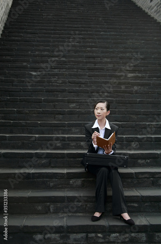 Businesswoman sitting on staircase holding organizer © ImageHit