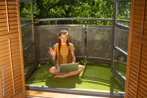 A young adult woman on video call at a laptop on her balcony in London during covid-19 lockdown