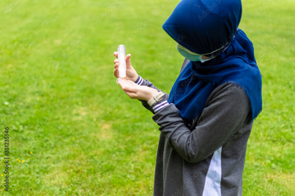 Muslim woman pouring liquid sanitizer on her hands