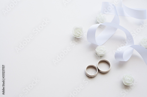 Wedding rings are decorated with a ribbon and white flowers with copy space. Concept backgrounds for weddings.