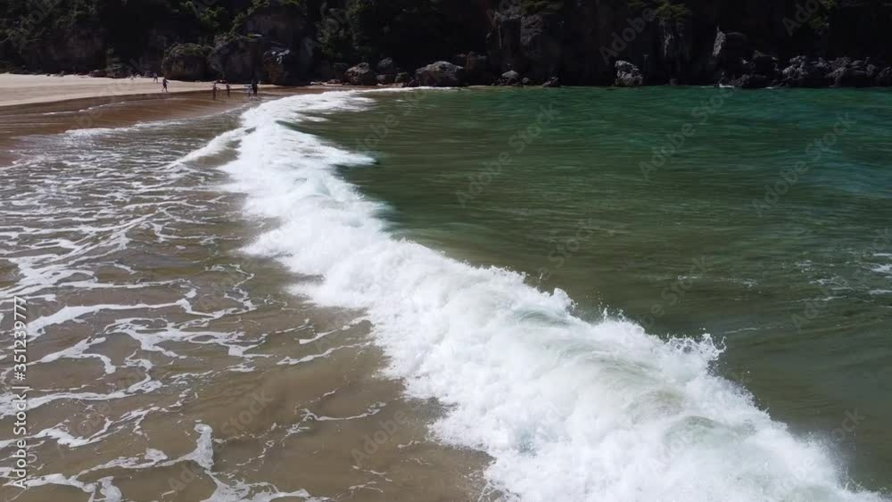 Pequeñas olas en la playa, la cámara acompaña en traveling lateral a la ola mientras se levanta y rompe hasta morir en la arena