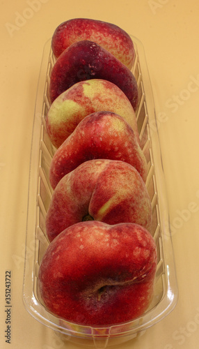 Foto closeup of plastic  punnet of ripe fresh fruit  flat peaches in a row isolated