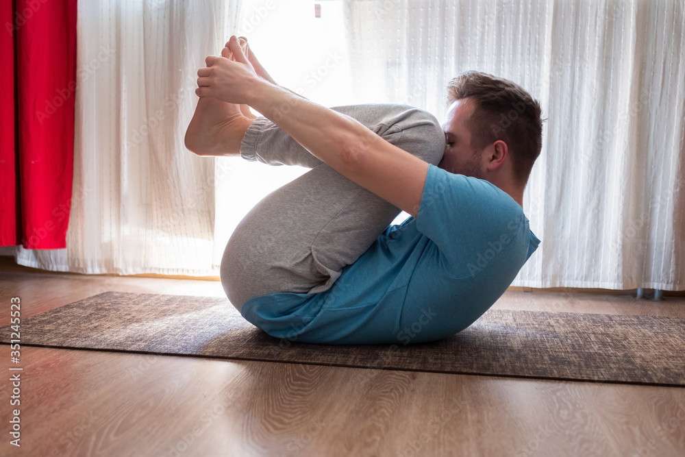 Caucasian man in Apanasana or Wind pose at home. Healthy lifestyle and wellness, recreation, sport concept