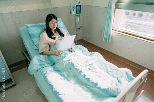 unhappy woman patient reading paper of bad test result while lying in hospital bed in room. cancer treatment oncology concept. depressed illness lady relax in recovery ward in sunshine clinic.