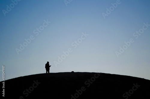 A person looks at his mobile while he is alone on top of a hill during a sunrise