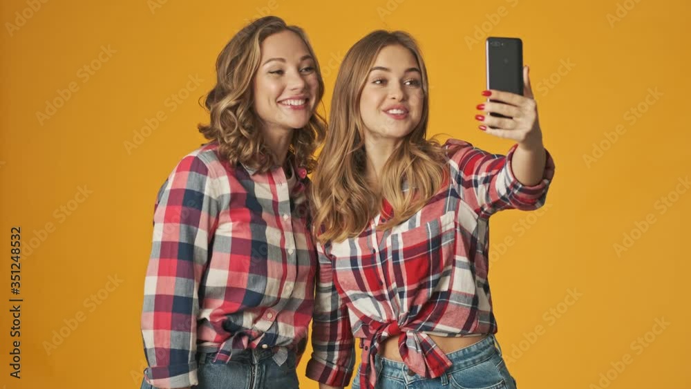 Young positive amazing girls isolated over yellow wall background talking by mobile phone by video call