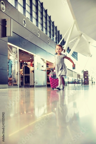 Portrait of young adorable little girl running in airport with her pink suitcase 