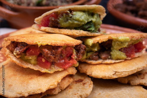 Vegan Mexican gorditas along with refried beans, guacamole, tomato salsa and fried seitan pieces in traditional Mexican bowls