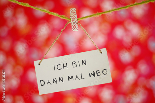 Ich bin dann mal weg, als Schriftzug auf weisser Tafel, hängt an einer Wäscheleine mit Wäscheklammer, vor einem fröhlichen, poppigen, buntem Hintergrund. 