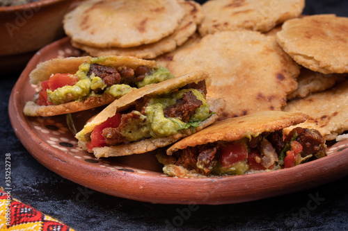 Vegan Mexican gorditas along with refried beans, guacamole, tomato salsa and fried seitan pieces in traditional Mexican bowls