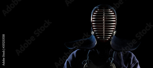 Male in tradition kendo armor with Samurai sword katana on black background. (unrecognizable person, dark mask) Shot in studio. Isolated with clipping path. Panoramic image.