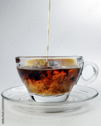 dark Coffee poring white milk dripping splash shadow liquid swirl in glass cup saucer on white background