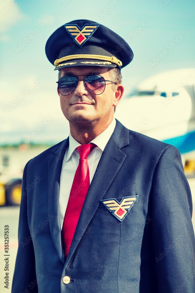 Portrait of mature pilot standing against airplane in airport
