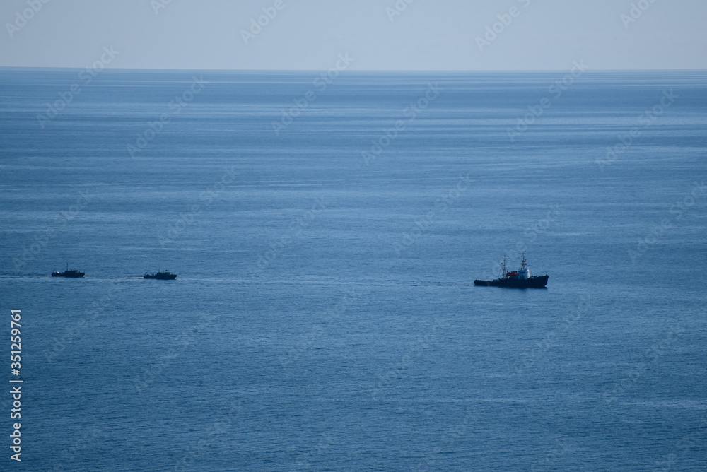 A large sea ship is sailing, and two small ships are sailing behind it, in a calm blue sea