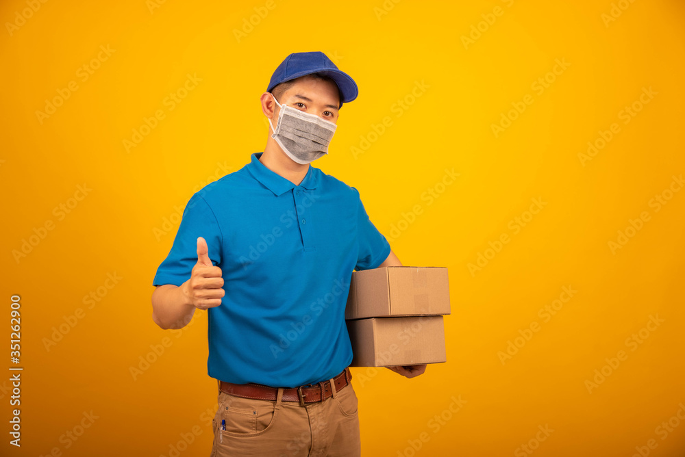 Delivery man wearing blue polo-shirt uniform face mask hold box on yellow background studio , coronavirus virus concept. Delivery man wearing blue polo-shirt uniform face mask hold box on yellow background studio , coronavirus virus concept.