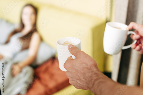 selective focus of man holding white cups near woman in bed