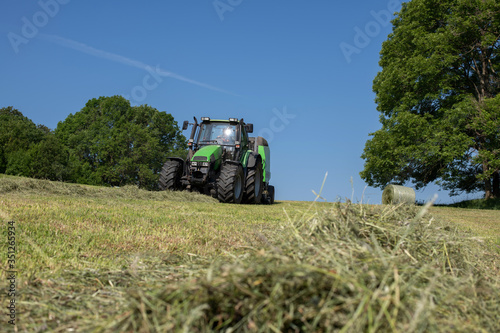 erster Grasschnitt, Traktor und Ballenpresse bei der Arbeit,
ernten und fertigen von Rundballen bei schönem Frühlingswetter photo