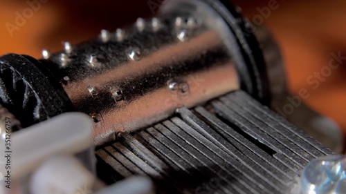 Music box drum clockwork mechanism close up on turning barrel and cogs. Old music box mechanism, rotating cylinder closeup. Toy barrel organ rotates, closeup view at orange background