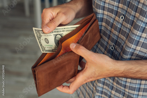 A close-up of a man's hand pulls out a 1 US dollar bill in his wallet photo