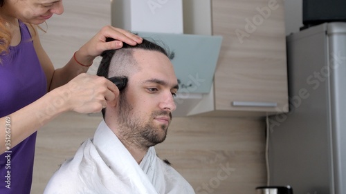 Portrait of attractive man gets haircut at home, during coronavirus or covid-19 isolation measures. Stay at home quarantine coronavirus pandemic prevention. Wife uses a hair clipper