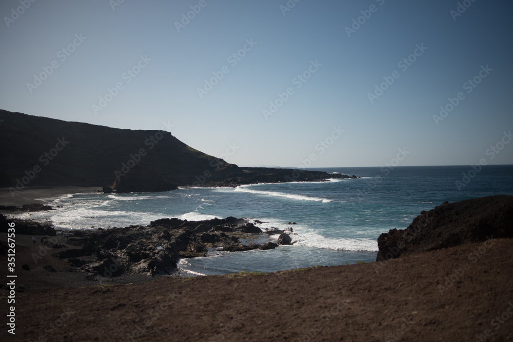 Aerial view of the rocky coastline of Lanzarote island with crushing waves on a sunny day with a blue sky 