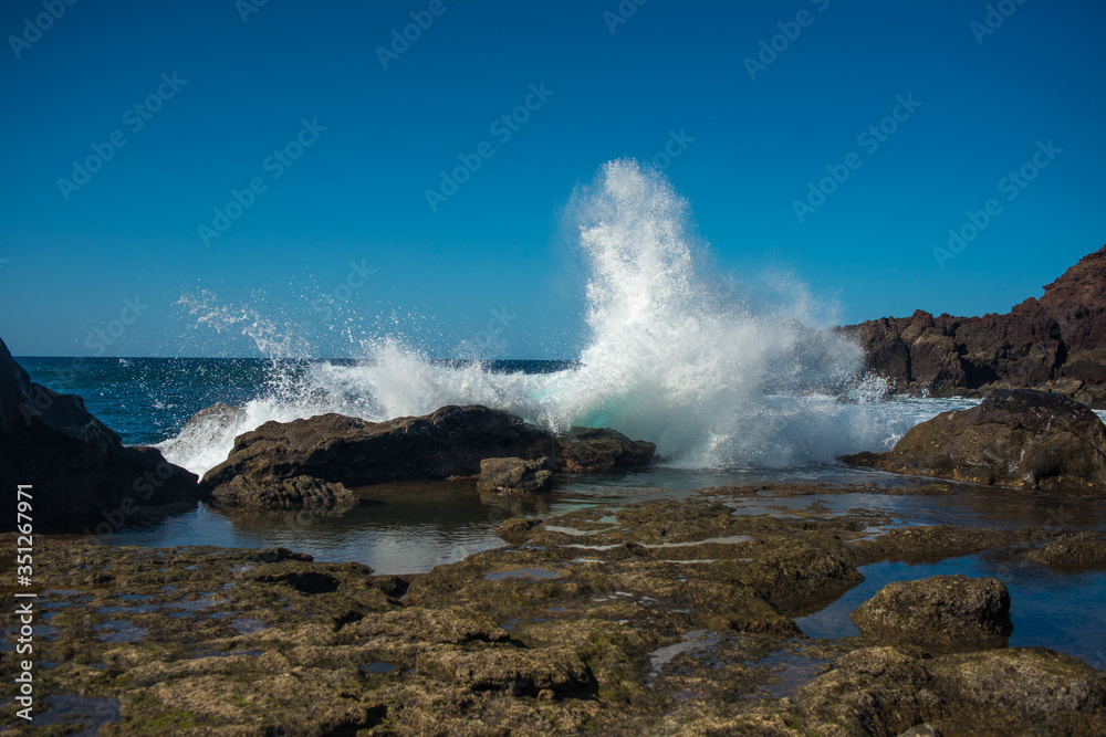 the rocky seaside of Lanzarote island with crashing waves on a sunny day with a blue sky 