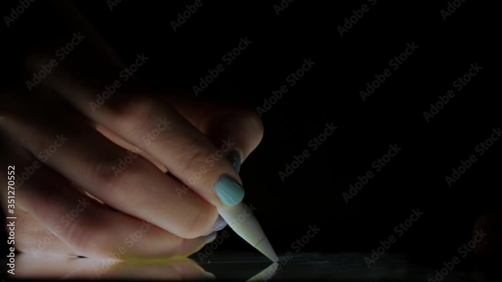 Close up hand of artist drawing on a digital tablet with pencil in dark room without light.