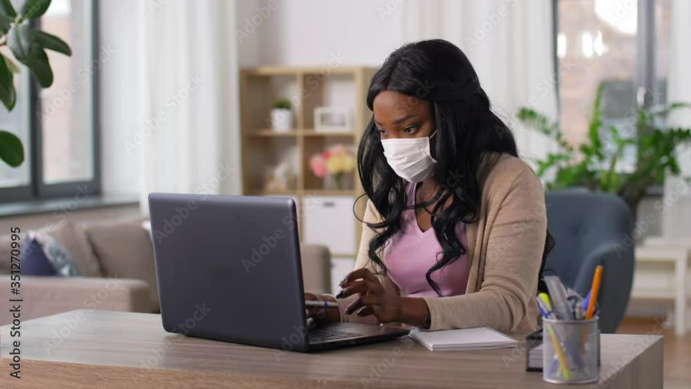 quarantine, remote job and pandemic concept - african american woman wearing face protective medical mask for protection from virus disease with laptop computer and notebook working at home office