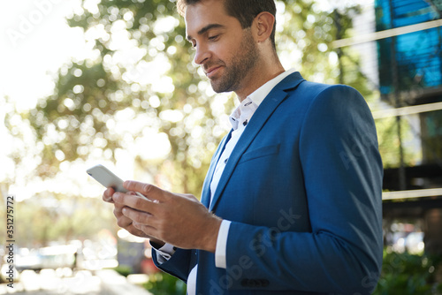 Young businessman standing outside sending a text on his cellphone