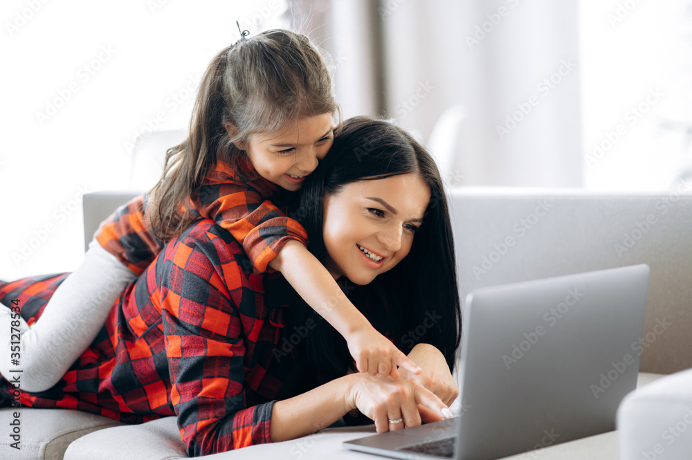 Online shopping. Joyful and pretty caucasian mom and daughter are shopping online at home on the couch using a laptop. Nice time together at home Online shopping. Joyful and pretty caucasian mom and daughter are shopping online at home on the couch using a laptop. Nice time together at home