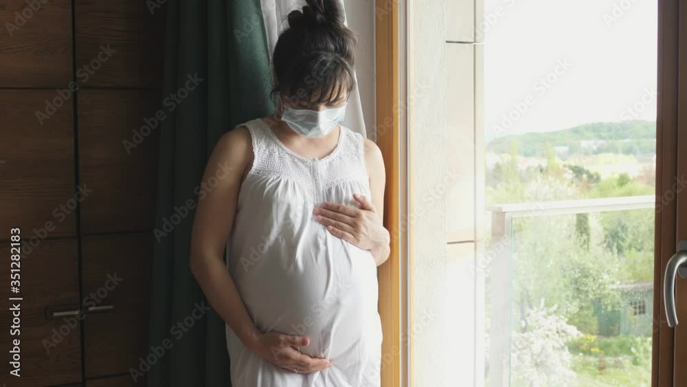 pensive pregnant woman in a protective mask looks out the window pensive pregnant woman in a protective mask looks out the window