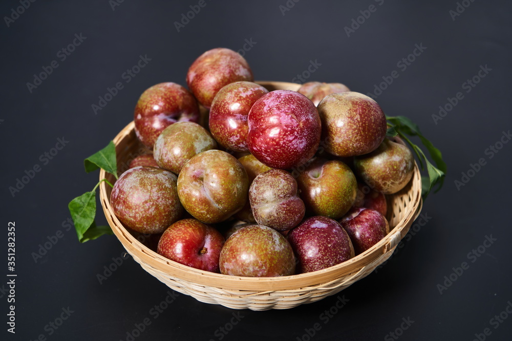 Fresh plums in a woven bamboo basket against a black background Fresh plums in a woven bamboo basket against a black background