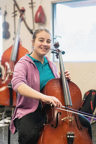 Portrait of smiling teenage girl playing cello in classroom