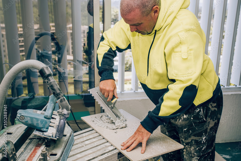 Professional builder smears cement glue on the ceramic tile with a trowel. Concept renovation repair, overhaul, contract tiler. Professional builder smears cement glue on the ceramic tile with a trowel. Concept renovation repair, overhaul, contract tiler.