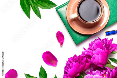 Beautiful flowers peonies, cup of coffee, green notebook, phone, pen on a white background top view with copy space. Female desktop, planning, morning coffee